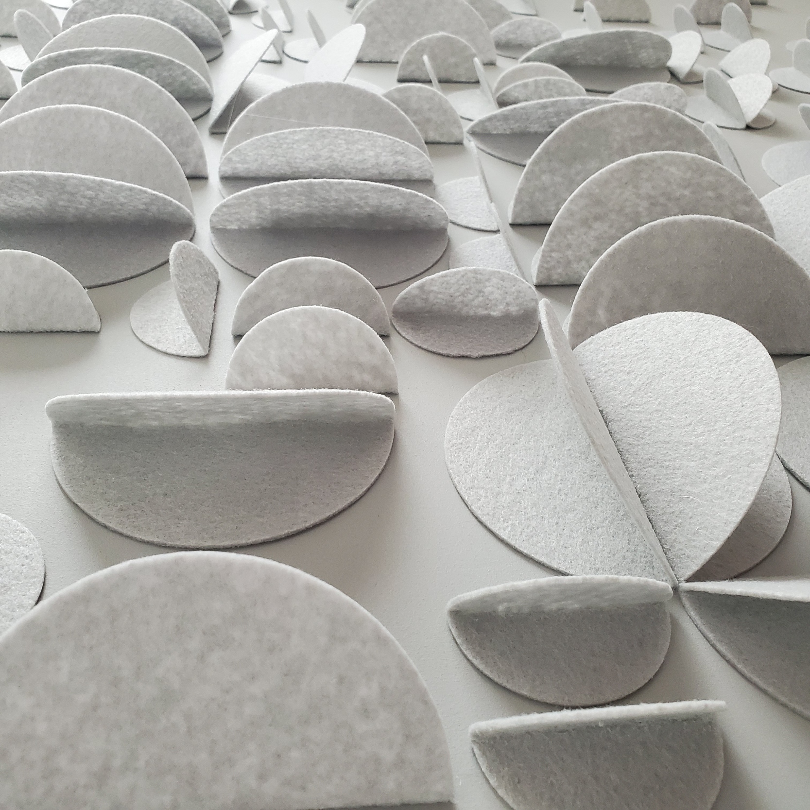 gray felt circles folded and mounted next to each other on wood panel